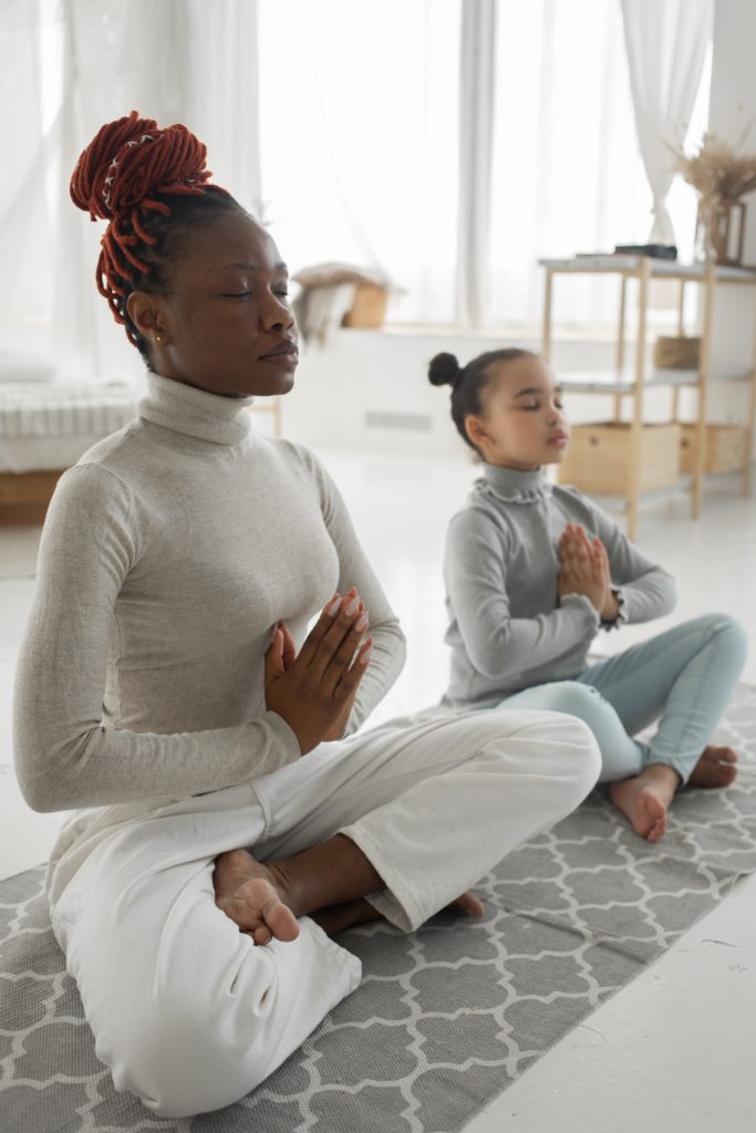Relaxed woman with little daughter practicing Lotus pose at home
