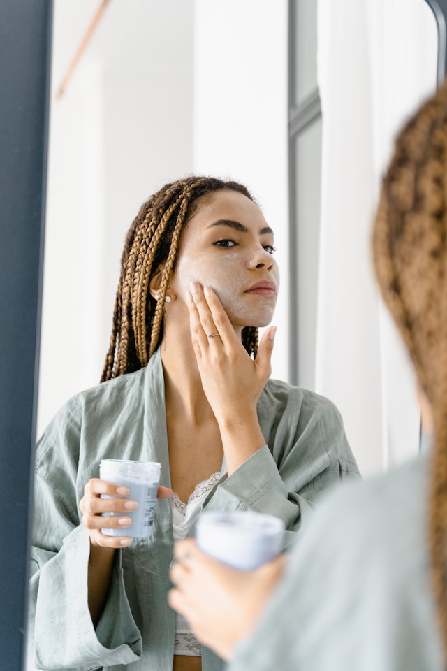 woman looking in mirror putting on facial moisutizer