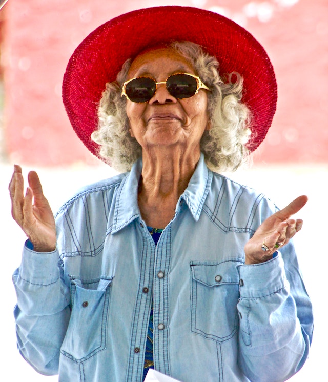 wise older woman in hat holding up her hands