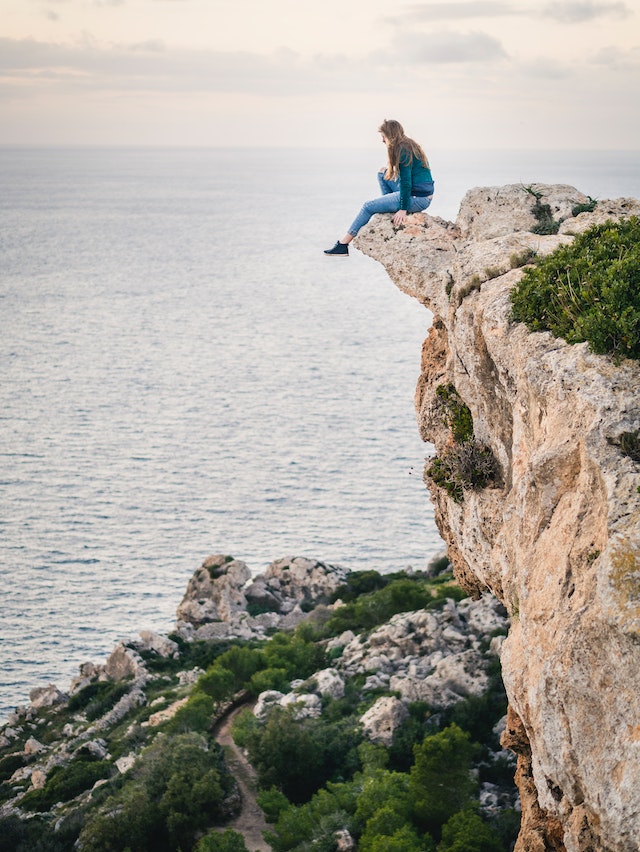 woman sitting on clif overlooking water
