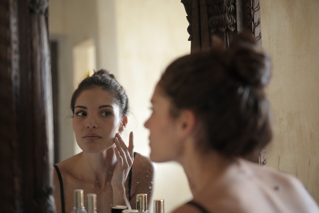 women looking in mirror picking at blemish