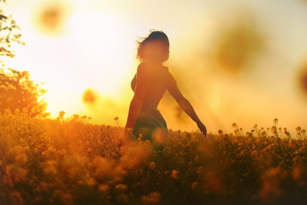 Silhouette of a woman in a field at sunset, enjoying the warm golden light. A visual representation of romanticizing life by savoring simple moments and embracing nature.