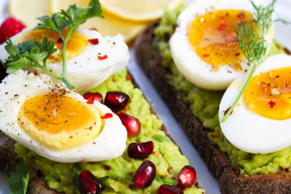 High protein breakfast idea with avocado toast topped with boiled eggs and herbs.