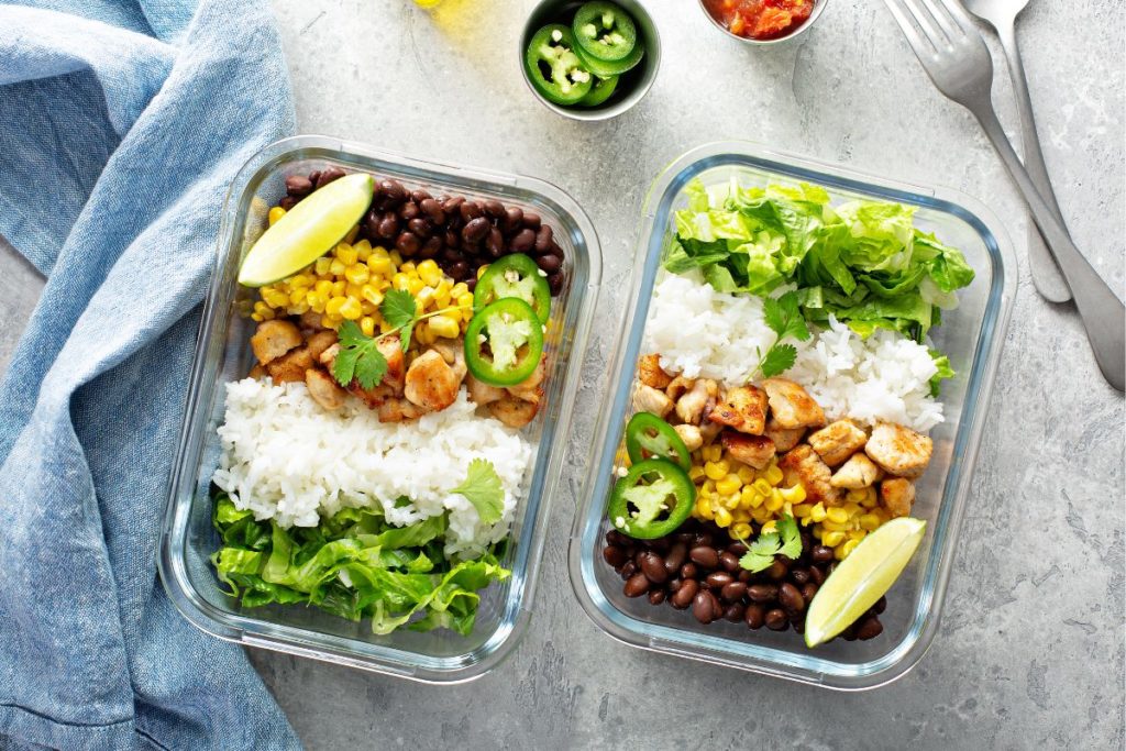 Healthy lunch meal prep ideas with rice, chicken, black beans, corn, and fresh greens in glass containers.