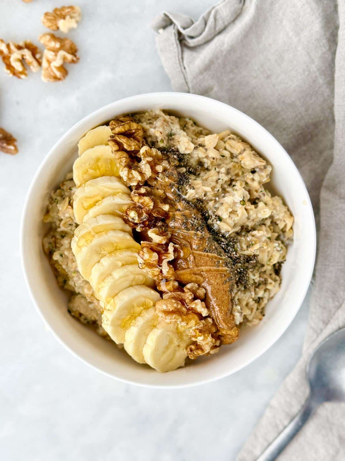 Bowl of protein oats topped with banana slices, walnuts, and nut butter