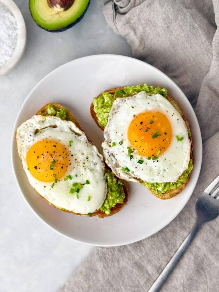 Two slices of avocado toast topped with fried eggs