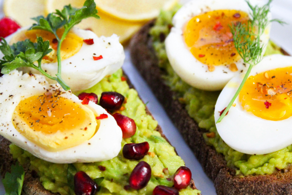 High protein breakfast idea with avocado toast topped with boiled eggs and pomegranate seeds.