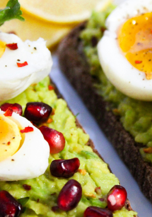 High protein breakfast idea with avocado toast topped with boiled eggs and pomegranate seeds.