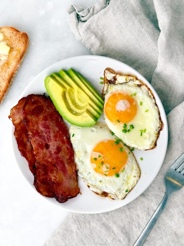 Plate with fried eggs, turkey bacon, sliced avocado, and toast