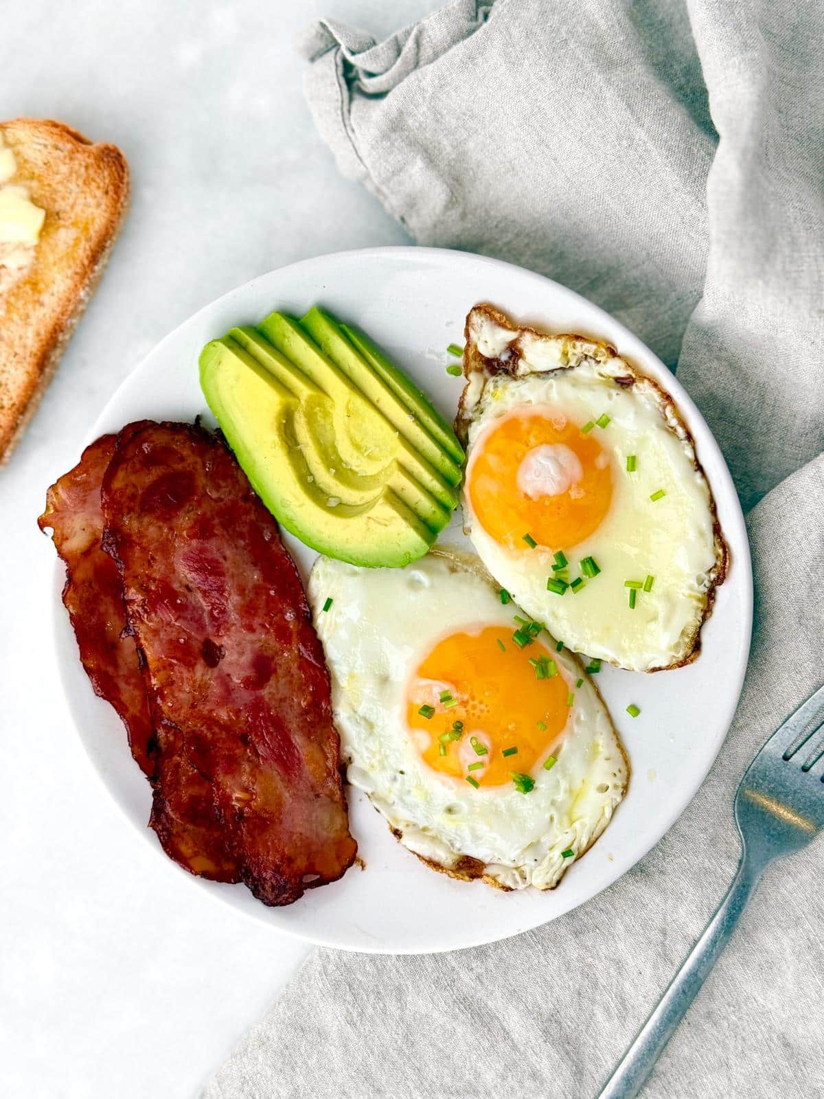 Plate with fried eggs, turkey bacon, sliced avocado, and toast
