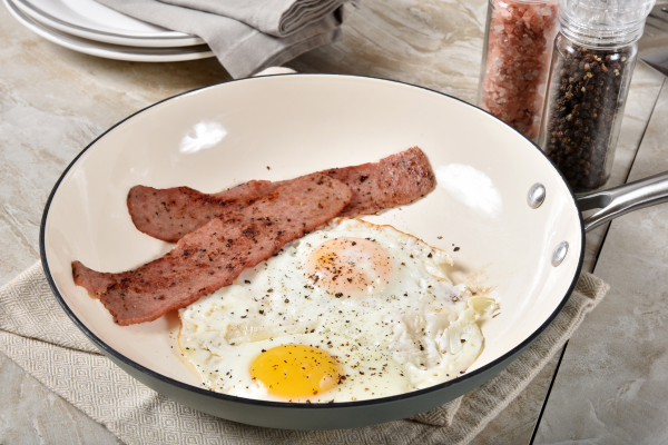 Fried eggs served with turkey bacon in a skillet as a high protein breakfast.