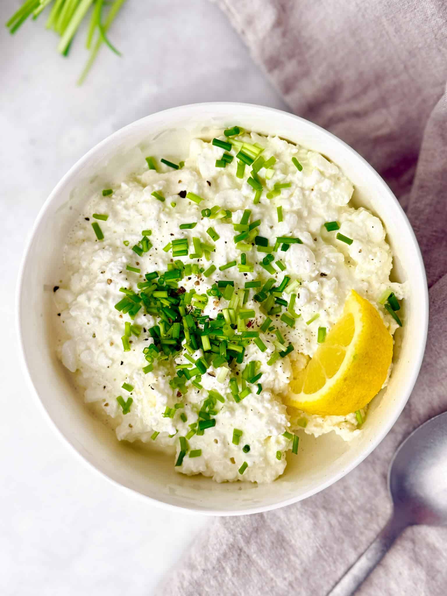 Bowl of savory cottage cheese topped with fresh chives and a lemon wedge