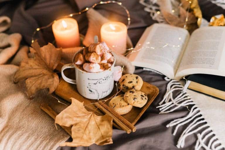 Cozy fall self-care scene with hot chocolate, cookies, candles, and a book for autumn relaxation.