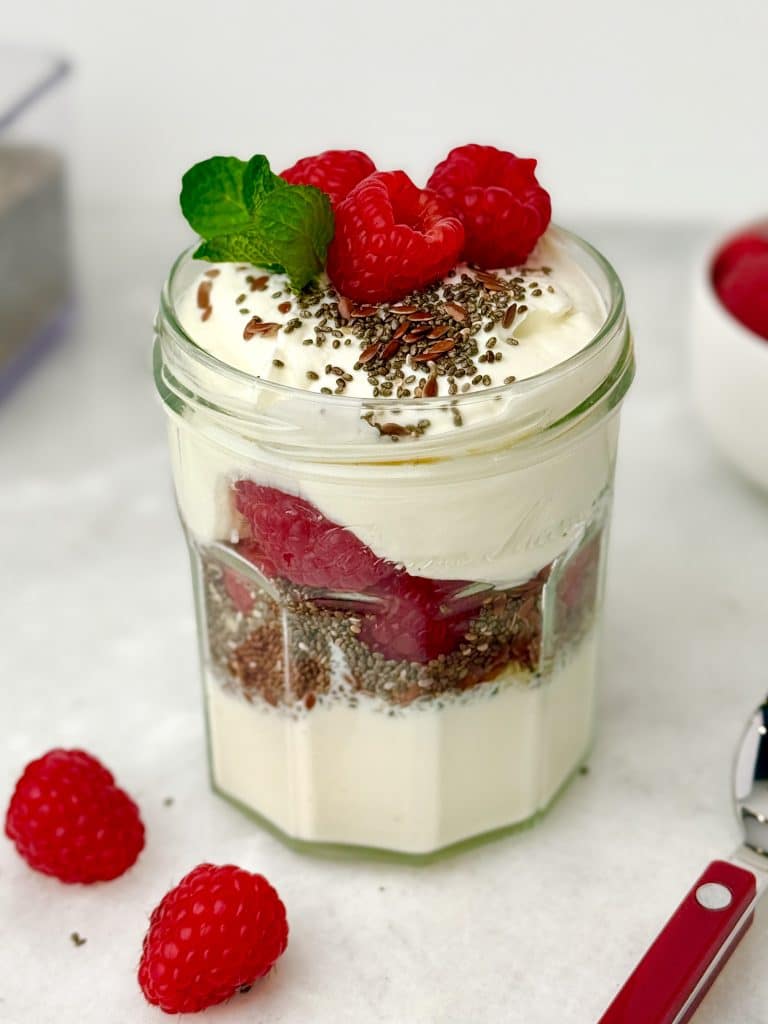High-protein low-carb Greek yogurt parfait layered with chia seeds, flaxseed, and fresh raspberries in a glass jar