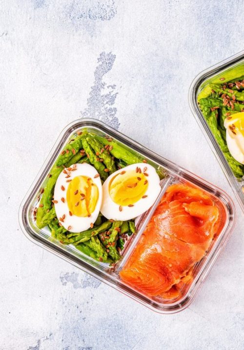 High protein lunch meal prep with boiled eggs, smoked salmon, asparagus, almonds, and cheese in a divided glass container