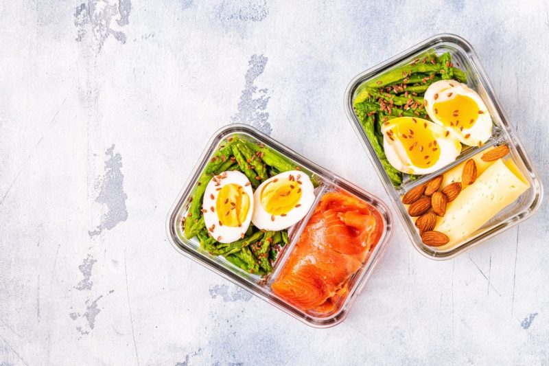 High protein lunch meal prep with boiled eggs, smoked salmon, asparagus, almonds, and cheese in a divided glass container