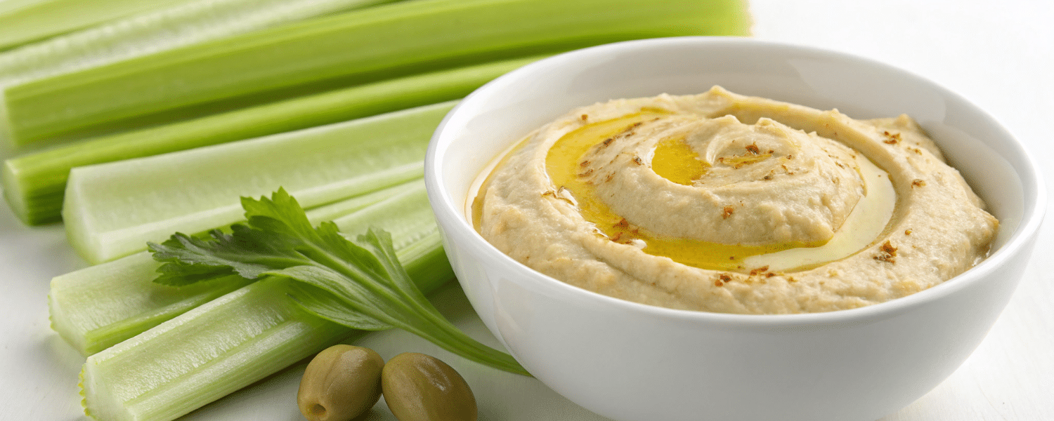 A bowl of hummus served with crisp celery sticks – a plant-based high-protein snack.