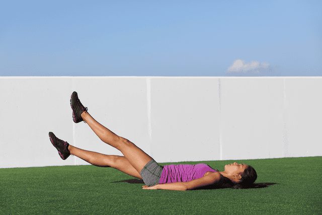 Woman doing flutter kicks, a deep core exercise that strengthens the pelvic floor and core muscles.