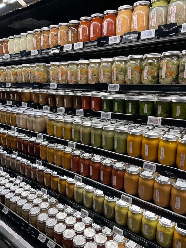 Shelves stocked with glass jars of soups and sauces at Erewhon Market, showcasing a variety of healthy fall dinner ideas like vegetable stews, broths, and comforting seasonal meals.