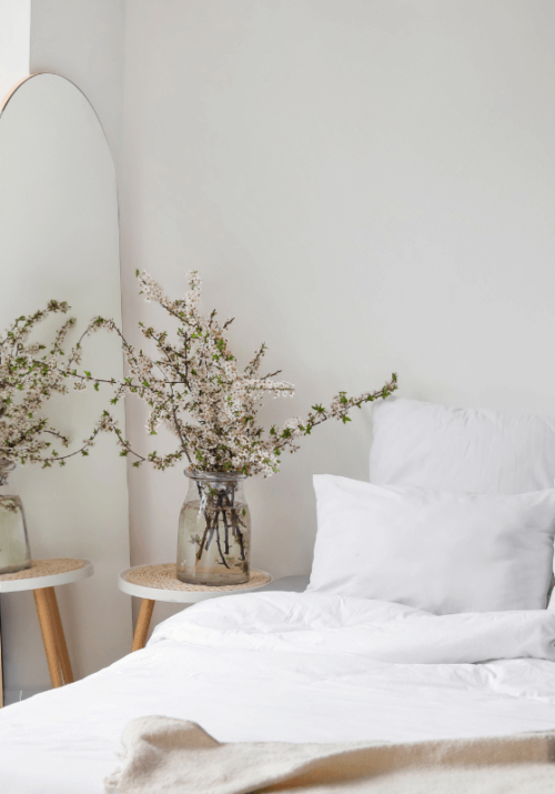 Cozy and minimalist bedroom with a large mirror, potted plants, and white bedding — perfect for a home bedroom refresh on a budget.