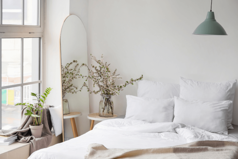 Cozy and minimalist bedroom with a large mirror, potted plants, and white bedding — perfect for a home bedroom refresh on a budget.