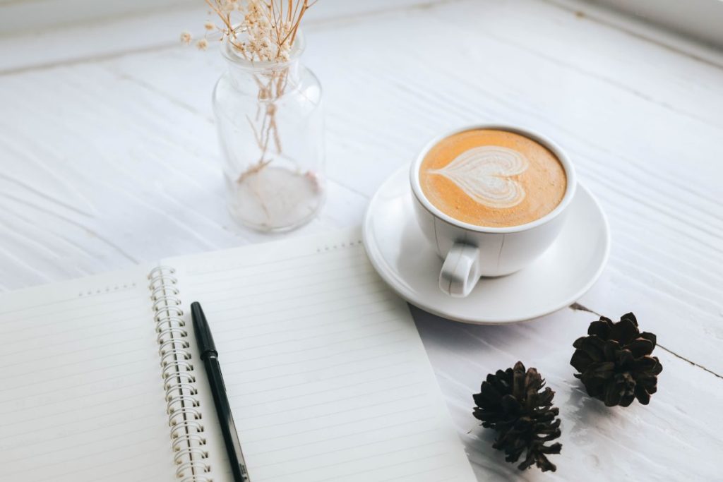 Open notebook with a pen beside a cup of coffee, perfect setup for planning goals list for 2025.