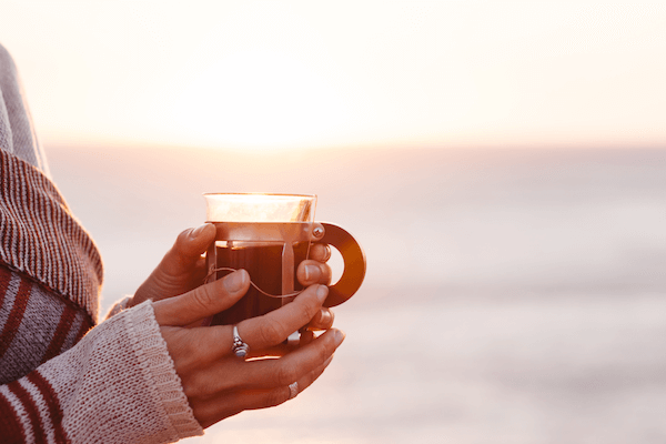 Person holding a cup of coffee while watching the sunrise as part of a screen-free morning routine.