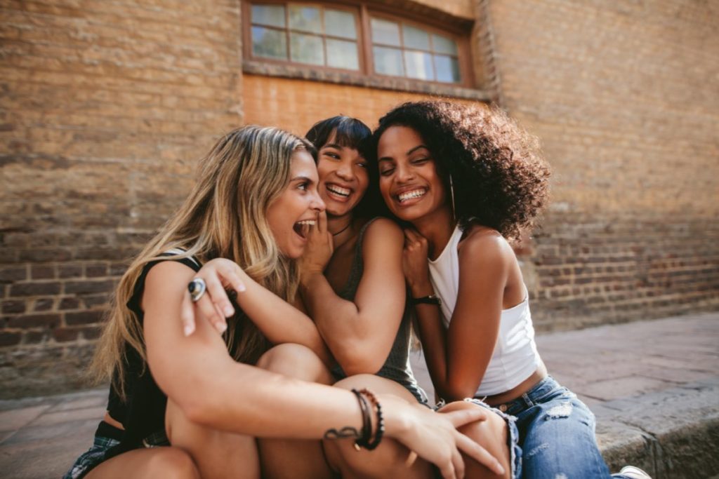 Three women making friends in a new city, sharing laughter and bonding outdoors.