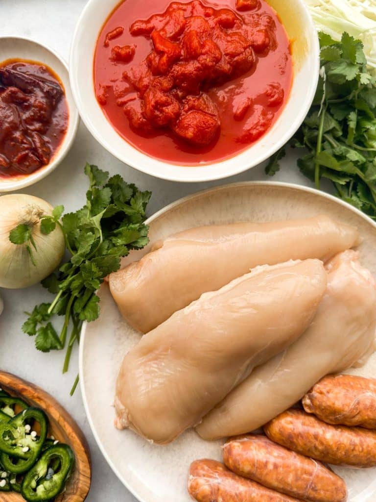 Chicken tinga slow cooker ingredients including chicken breasts, fire-roasted tomatoes, chipotle peppers in adobo, onion, and cilantro