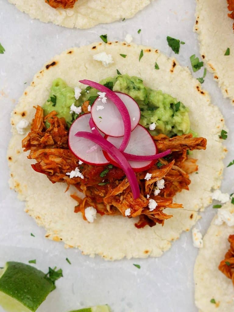 Close-up of a Guisados copycat chicken tinga taco with guacamole, sliced radishes, pickled red onions, and cotija