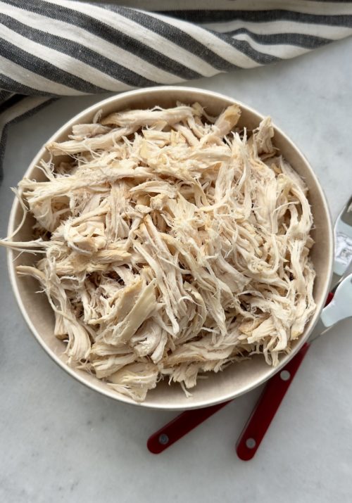 slow cooker shredded chicken in a bowl surrounded by a striped napkin and two forks used for shredding.