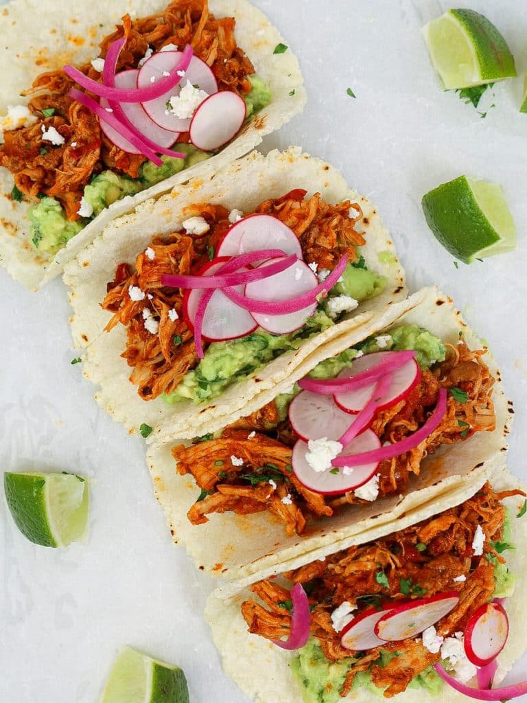 Tinga de pollo slow cooker tacos topped with guacamole, pickled red onions, sliced radishes, and cilantro