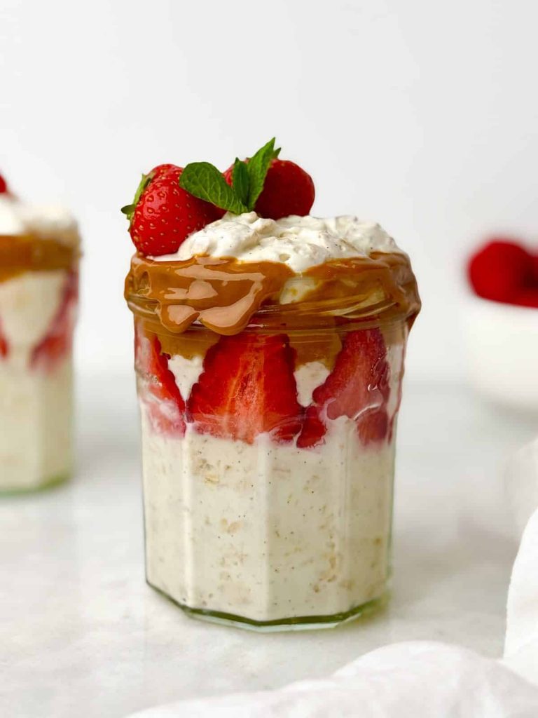 High-protein breakfast meal prep in a jar with creamy overnight oats, fresh strawberries, peanut butter drizzle, and mint.