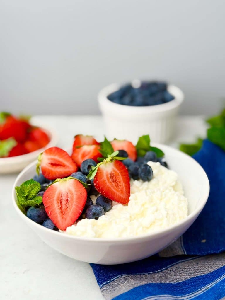 High-protein cottage cheese bowl topped with fresh strawberries, blueberries, and mint leaves, served on a blue linen napkin for a healthy breakfast.