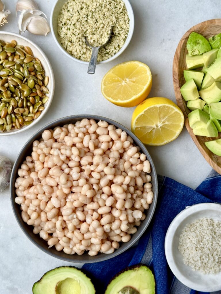 Fresh ingredients for an Erewhon kale white bean salad recipe, including white beans, pumpkin seeds, hemp seeds, chopped avocado, and lemon. A nutrient-dense mix perfect for a healthy kale and bean salad recipe.