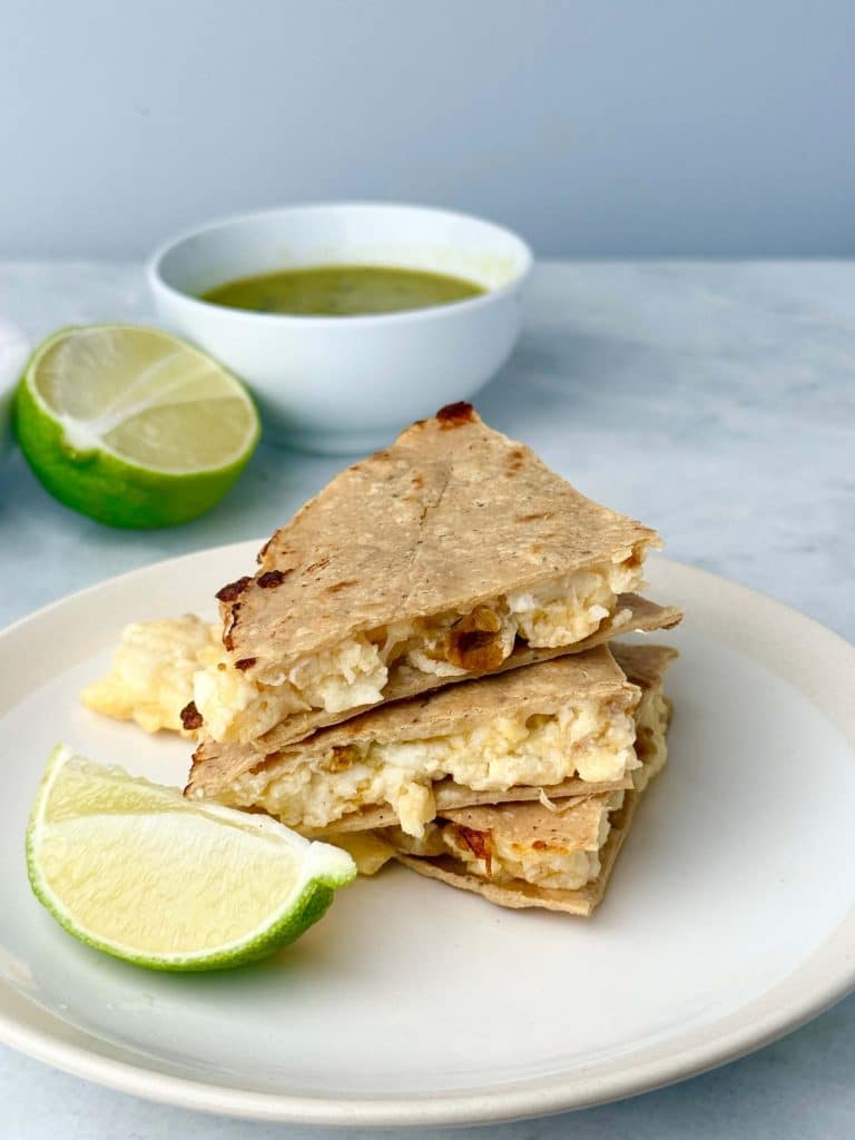 Stacked high protein breakfast quesadillas made with corn tortillas, egg whites, chicken sausage, and melted cheese, served with fresh lime and green salsa.