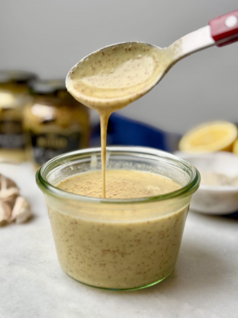 A creamy mustard dressing being poured into a glass jar, ready to be drizzled over an Erewhon kale white bean salad recipe. This dressing adds a tangy, rich flavor to the fresh kale and bean salad recipe.