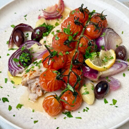 mediterranean chicken sheet pan dinner with chicken thighs, tomatoes, and olives.