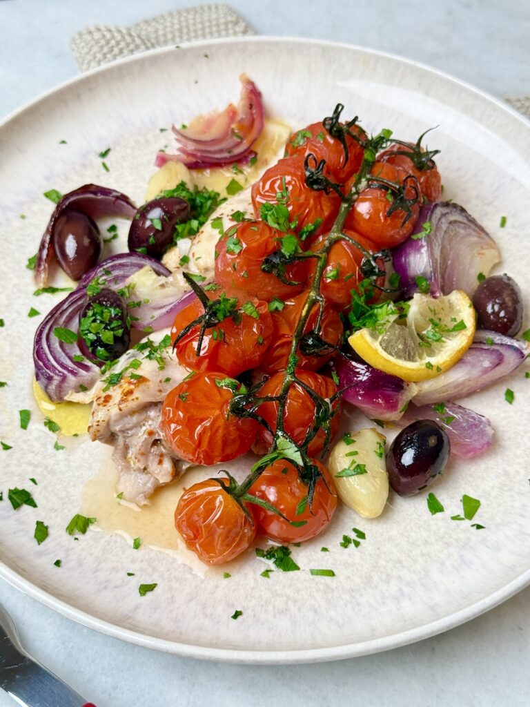 mediterranean chicken sheet pan dinner with chicken thighs, tomatoes, and olives.