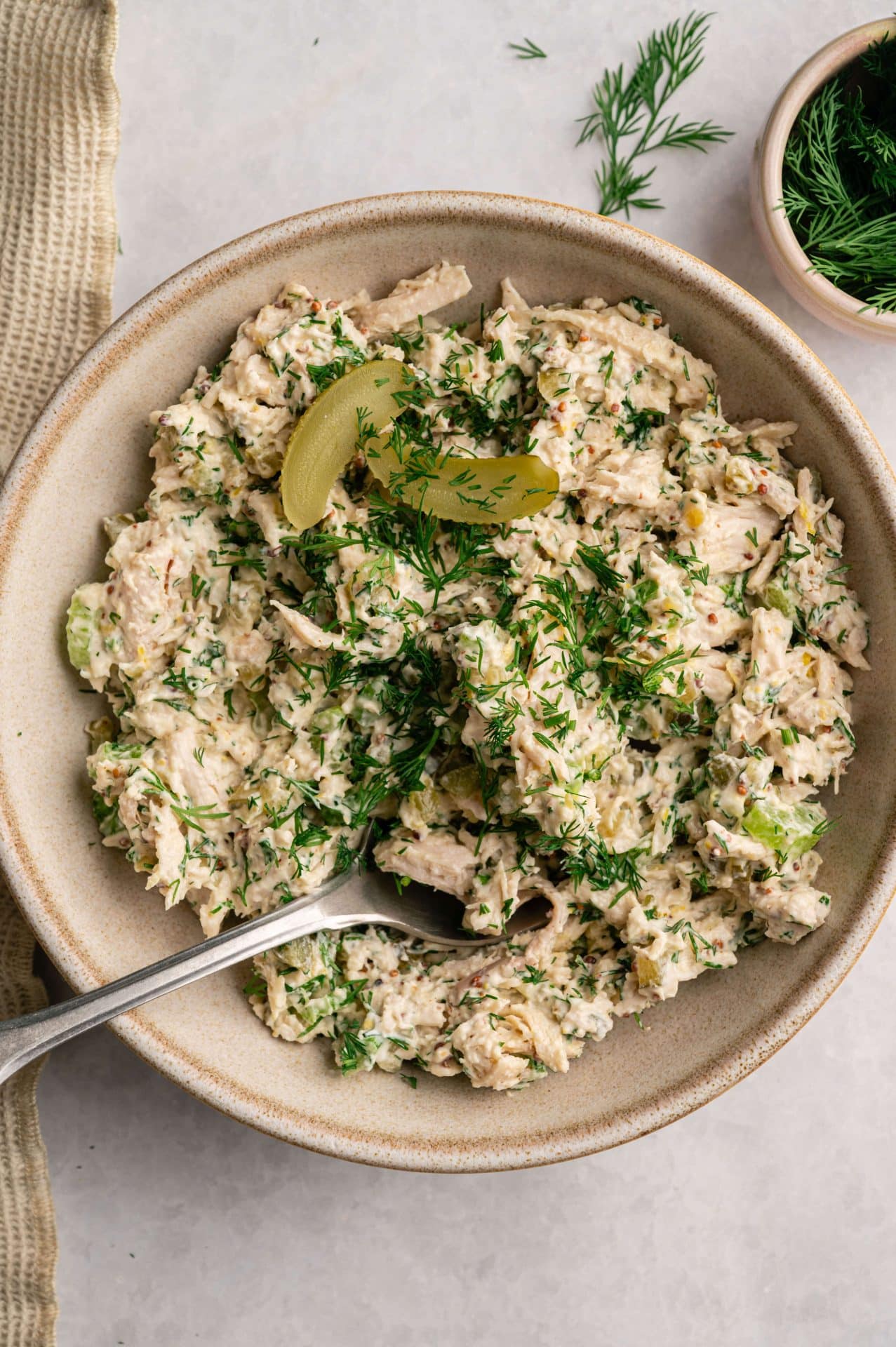 High protein dill pickle chicken salad served in a bowl with a fork, topped with fresh dill and pickle slices.
