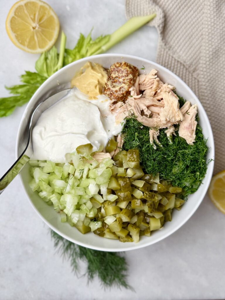 Fresh ingredients for dill pickle chicken salad including shredded chicken, chopped pickles, celery, dill, Greek yogurt, and mustard.