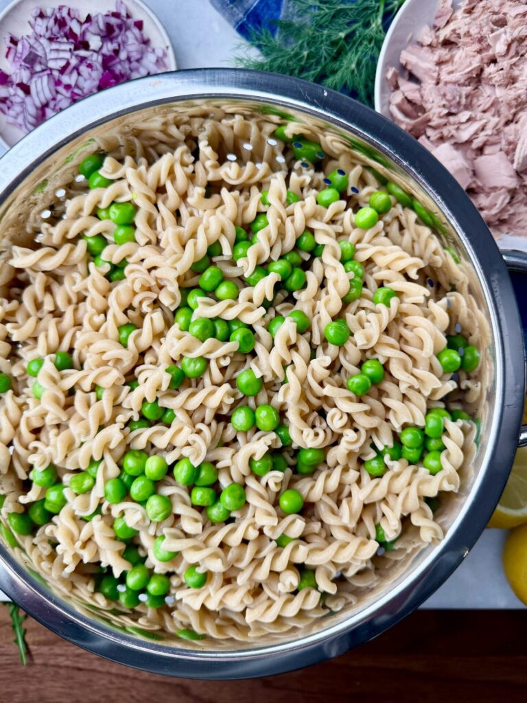 Whole wheat pasta and green peas in a strainer, ready for a high-protein tuna pasta salad.