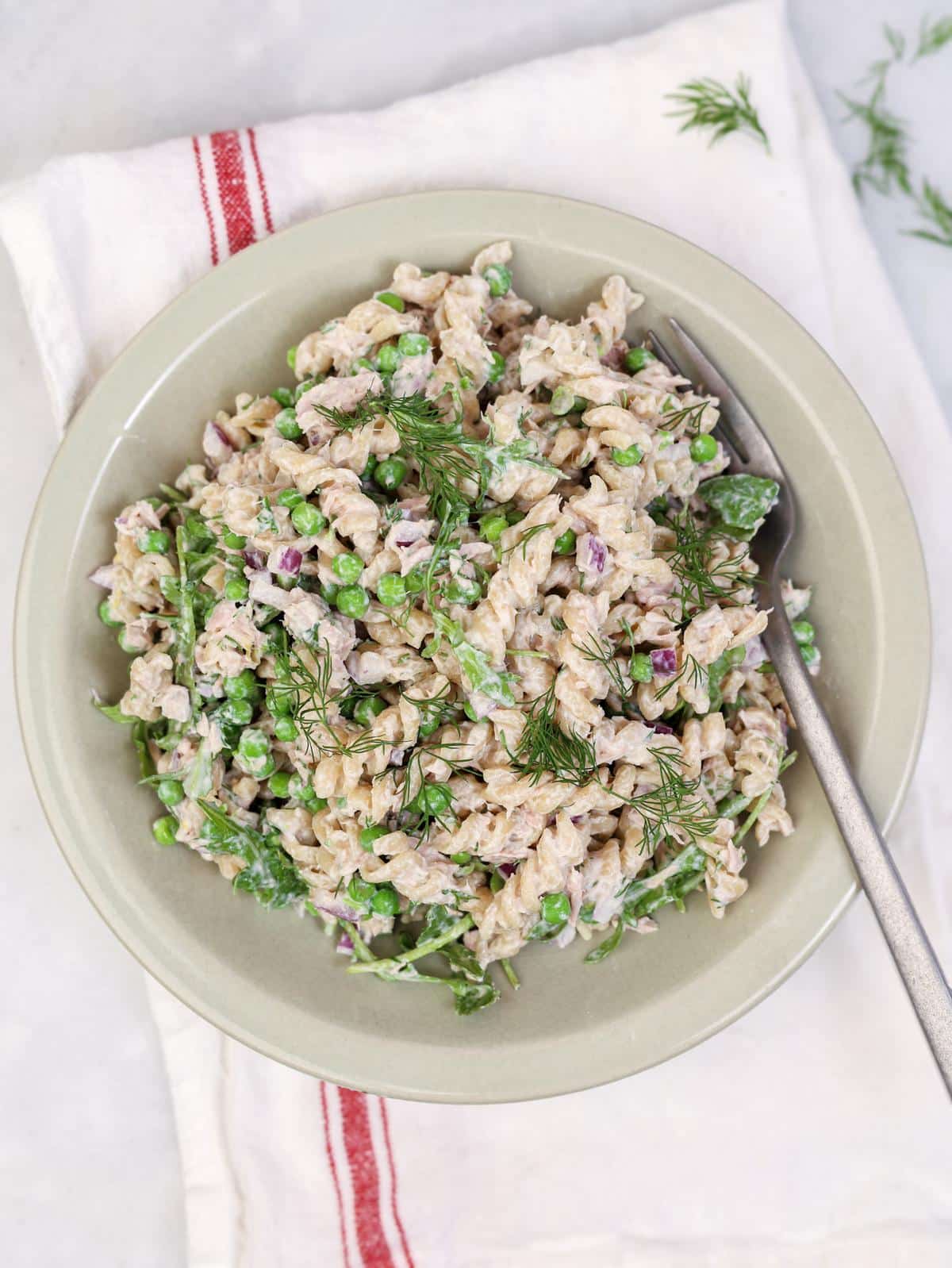 High-protein tuna pasta salad with peas, fresh dill, and creamy yogurt dressing in a green bowl