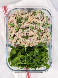 Tuna pasta salad meal prep in a glass container with fresh arugula on the side