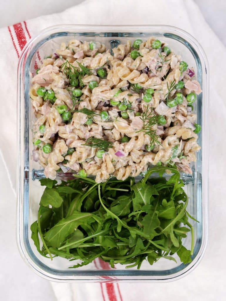 Tuna pasta salad meal prep in a glass container with fresh arugula on the side