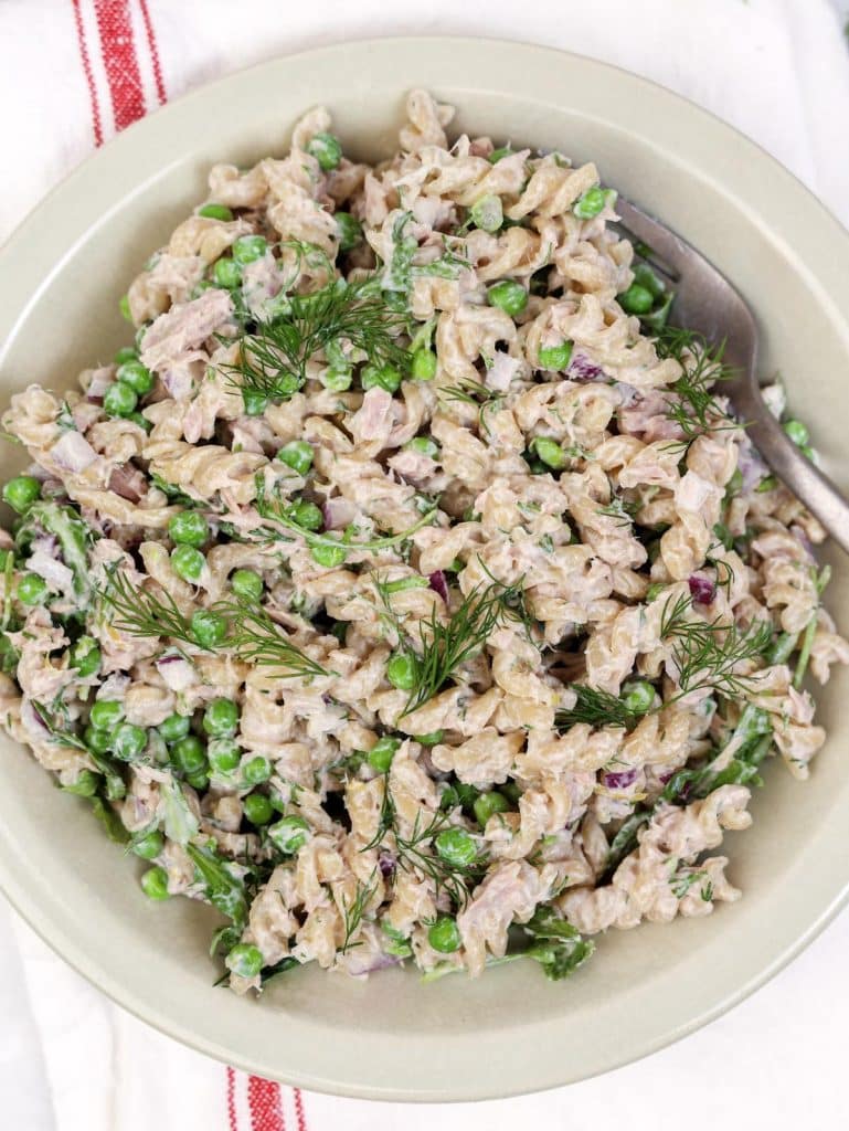 Close-up of protein tuna pasta salad topped with fresh dill and green peas