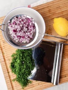 Red onion, fresh dill, and lemon for high-protein tuna pasta salad on a wooden board