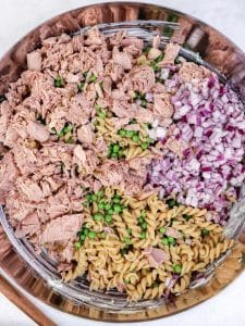 Tuna, peas, red onion, and pasta arranged in a bowl before mixing into a high-protein pasta salad