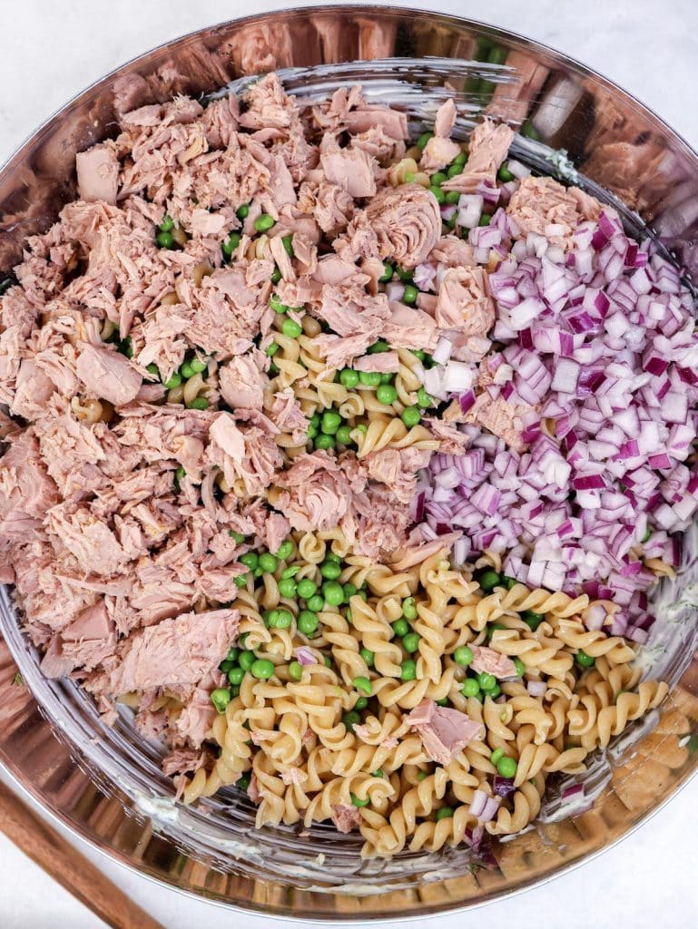 Tuna, peas, red onion, and pasta arranged in a bowl before mixing into a high-protein pasta salad