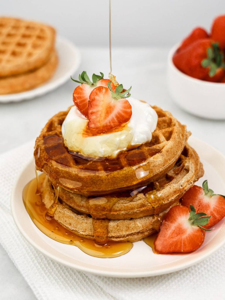 Easy high-protein breakfast ideas: stack of waffles topped with greek yogurt, strawberries and a maple syrup drizzle